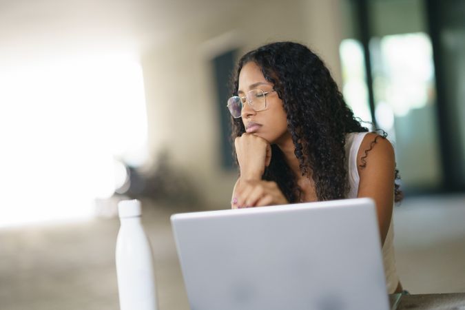 A Thoughtful and Contemplative Young Woman Engaged in Working on a Laptop in a Modern Workspace