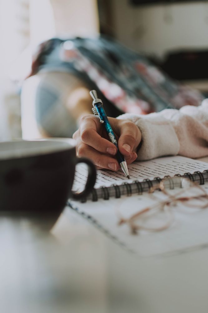 Cropped image of a hand writing on a notebook near mug
