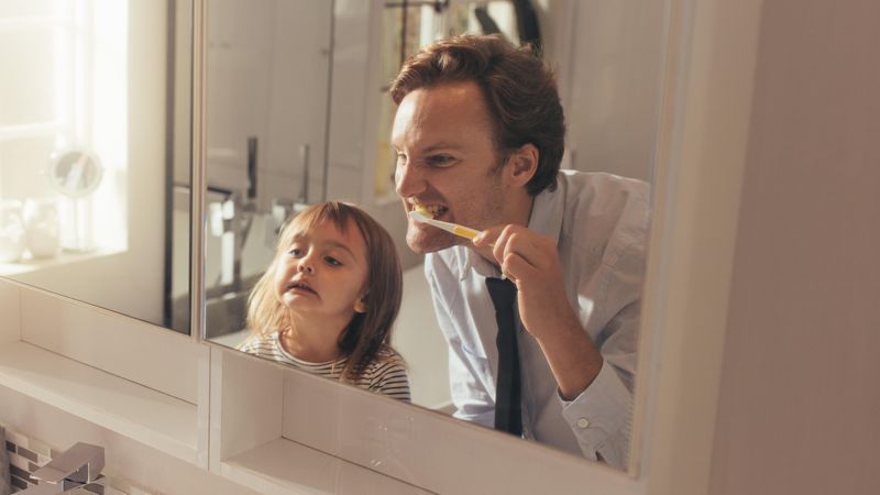 Man teaching his daughter how to brush teeth