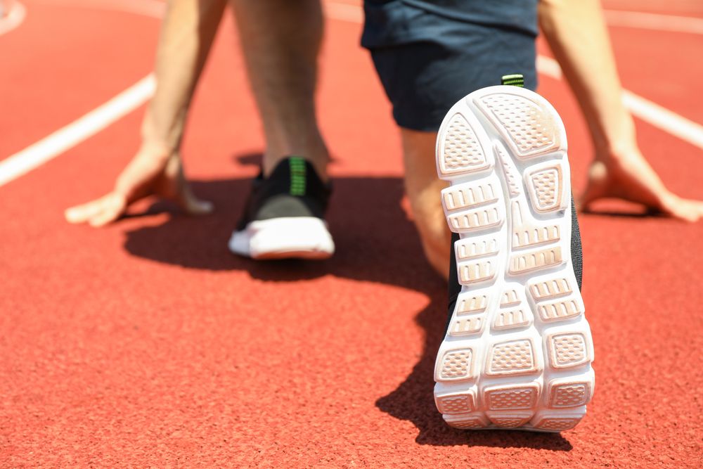 Sportsman low starting to run on red athletic track, close up