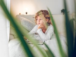 Dreamy calm preteen boy lying on sofa with tablet