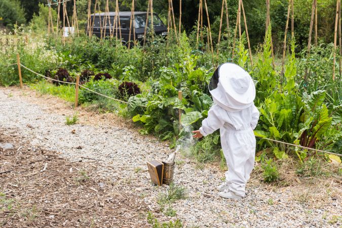 Child in protective costume standing near bee smoker