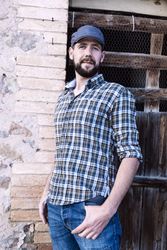 Casual man standing with his back against a brick wall while looking at camera