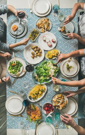 Group of people at blue patterned table with fresh fruits, salad, and vegetables with wine