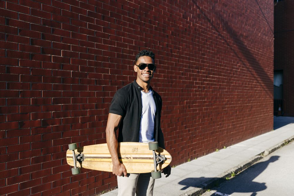 Young Black male with long board standing near wall