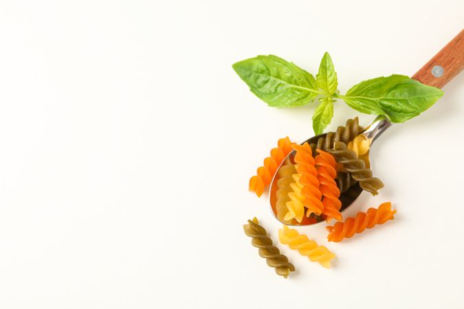 Spoon with color pasta on blank background, space for text and top view