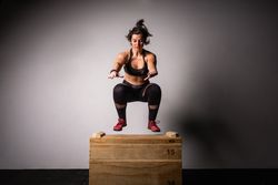 Woman jumping on wooden box in gym