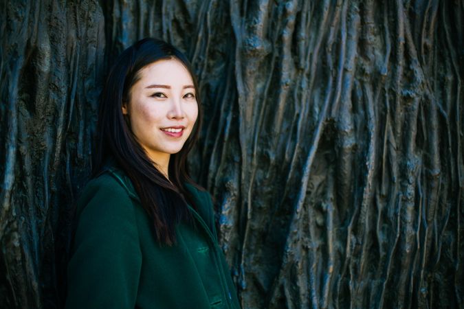 Cheerful Asian woman leaning on rough wall