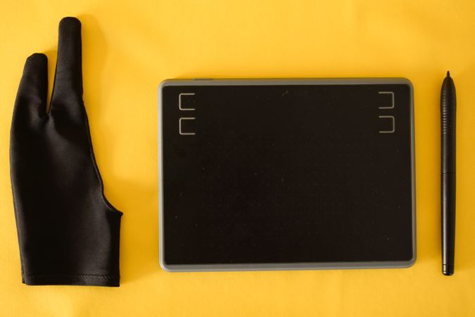 Top view of digital tablet, glove and stylus on yellow table with copy space