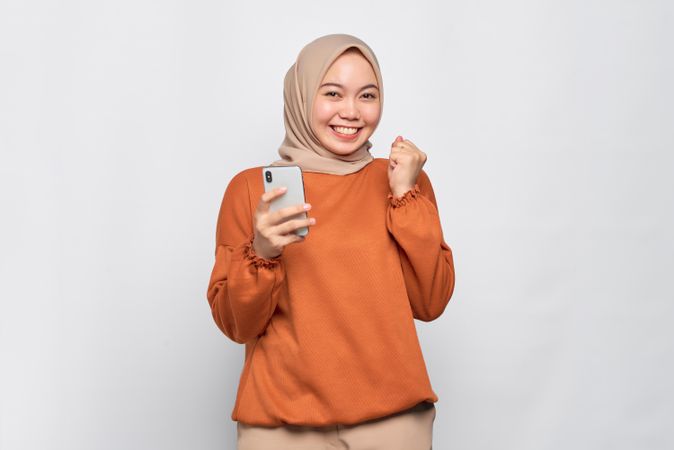 Smiling Muslim woman in headscarf and orange shirt receiving news that she won an phone