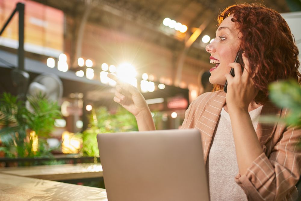 Young woman talking on phone while working on laptop
