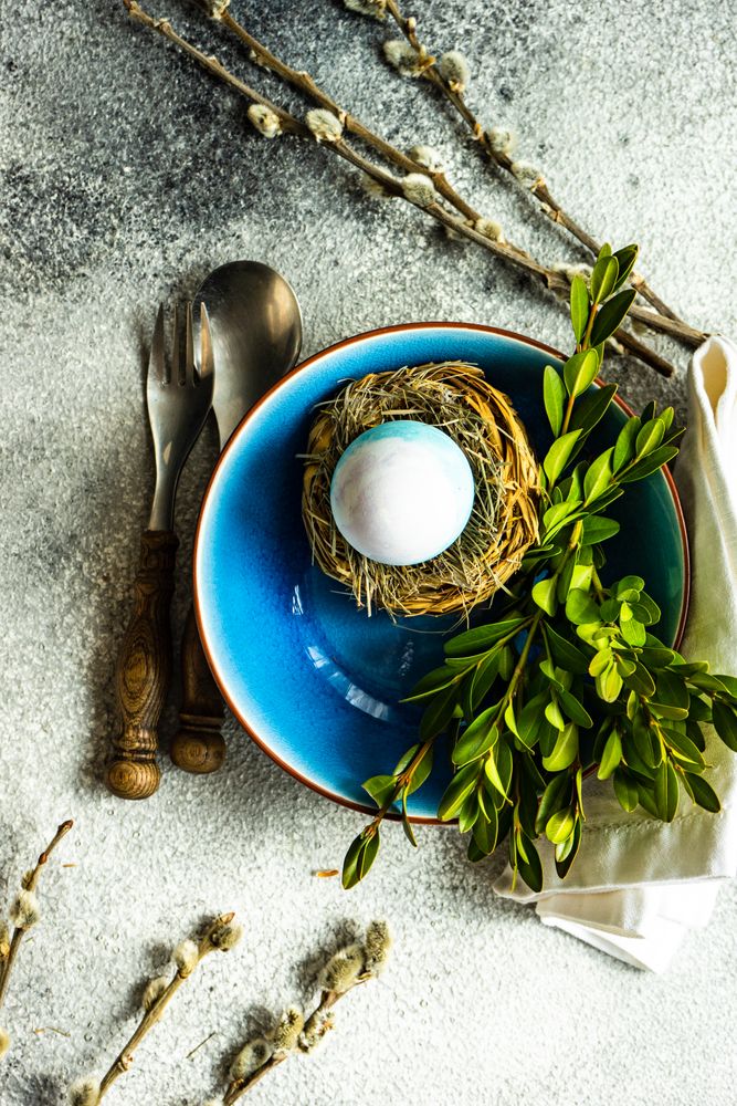 Top view of Easter table setting with blue bowl with decorative egg in nest