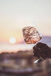 Man's hand swirling glass of rose wine against sunset, vertical composition