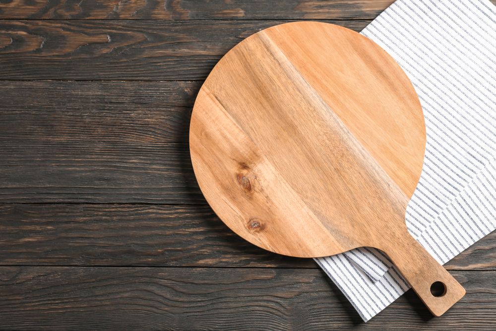 Cutting board with kitchen towel on wooden background, space for text