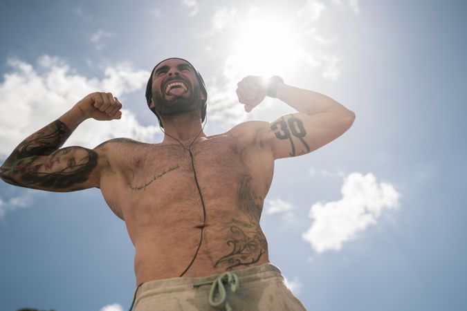 Sportsman flexing muscles against sky