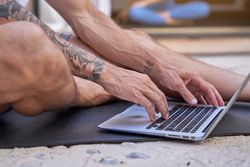 Crop tattooed man using laptop on mat