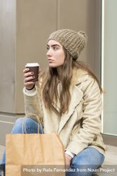Woman sitting outdoors holding a take away coffee after shopping 0LddvV