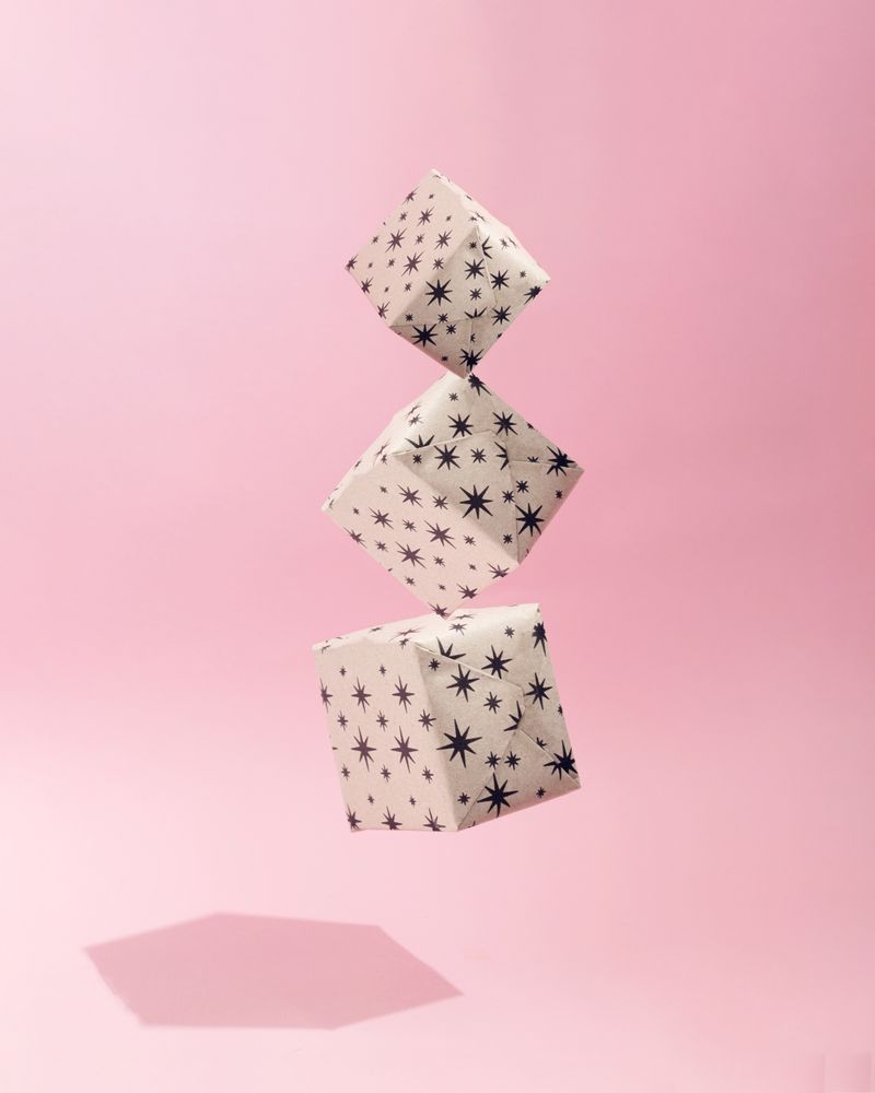 Three gift wrapped Christmas presents suspended on soft pink background with shadow