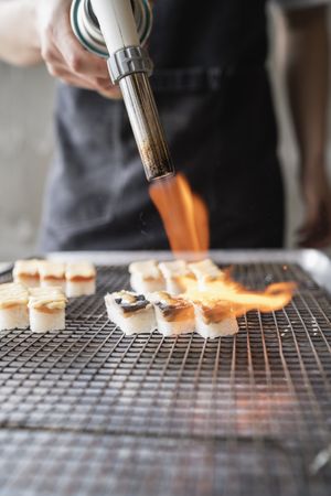 Male chef using culinary torch on sushi pieces