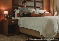 Businesswoman relaxing on bed reading newspaper in modern hotel room bEpzA4