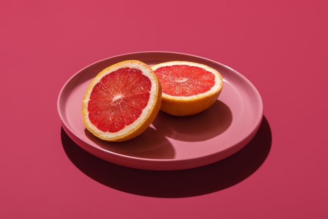 Grapefruit on pink plate, isolated on a magenta background