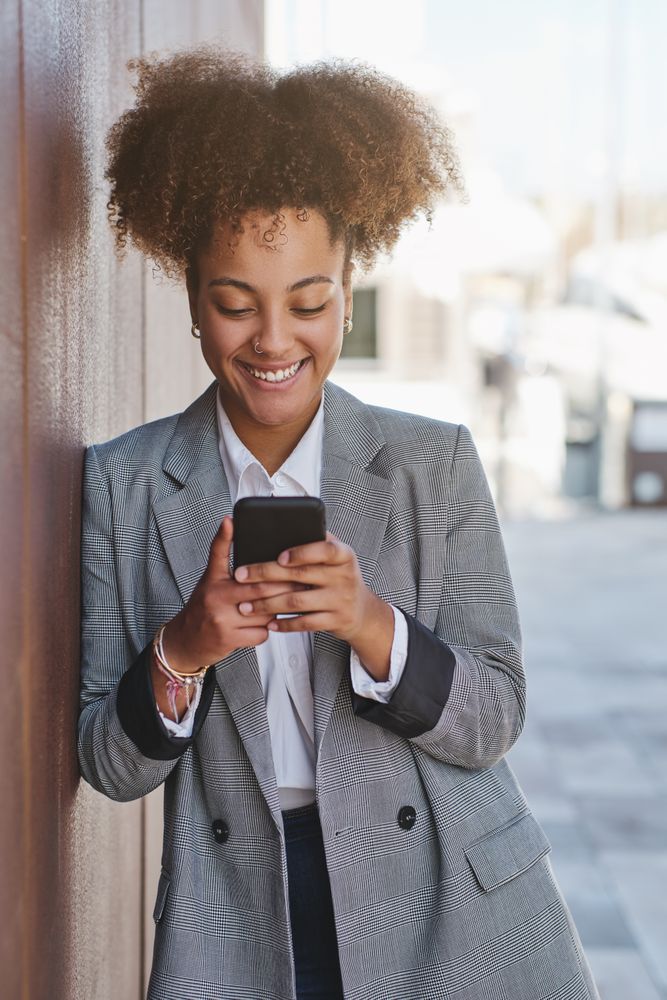 Carefree Black woman browsing smartphone on street