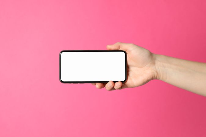 Female hand holds phone on pink background. Empty screen