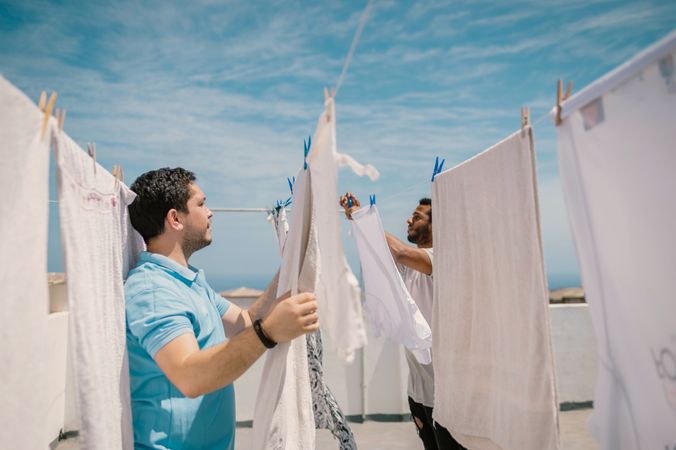 Multiracial men hanging clothes in bright day