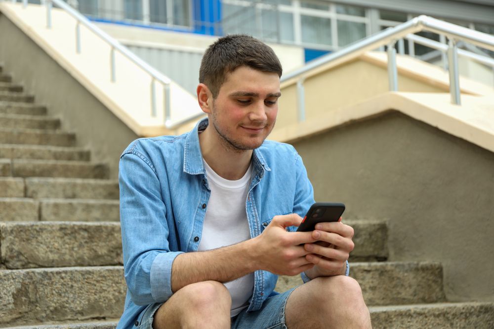 Young man sits on the steps and looking in phone