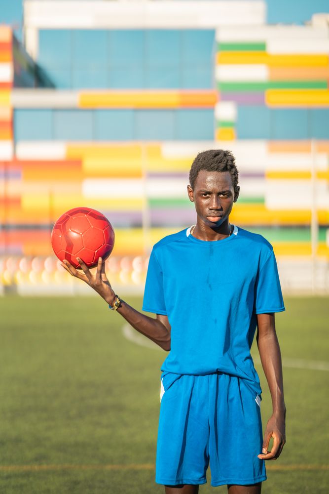 Black teenager with football ball against sky