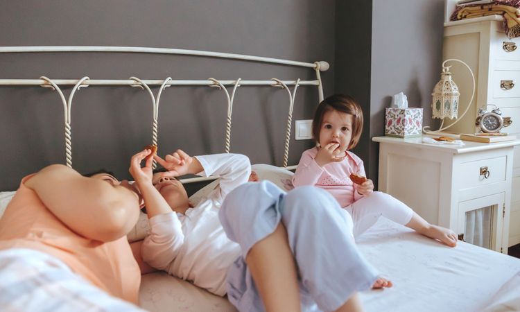 Portrait of happy little girl eating cookies in bed next to her mother and brother