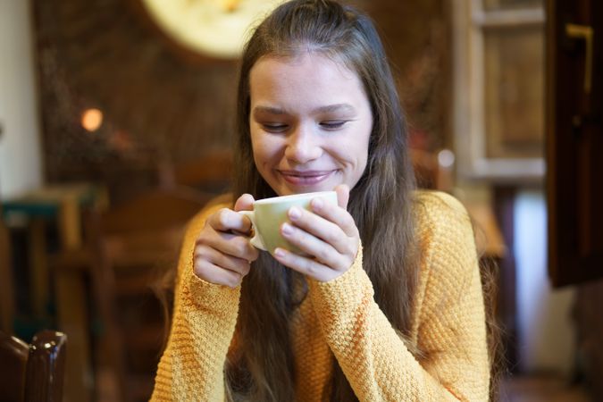 Joyful Young Woman Enjoying a Cup of Coffee in a Cozy Caf