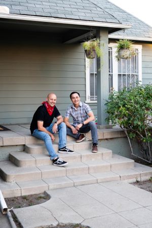 Portrait of cheerful married couple sitting on steps in front of a house smiling