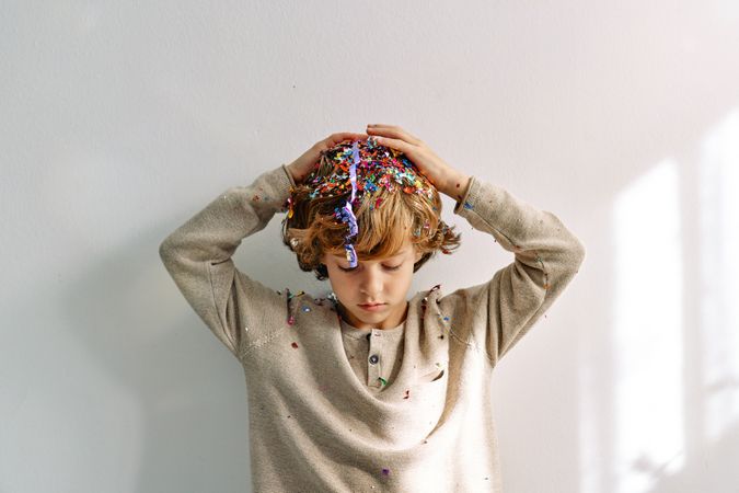 Sad little boy with drooping head covered with confetti