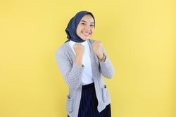 Excited Young Asian Female Wearing Scarf with Raised Hands Celebrating Success.