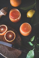 Two glasses of freshly squeezed blood orange juice, with squeezer, and fruit, top view
