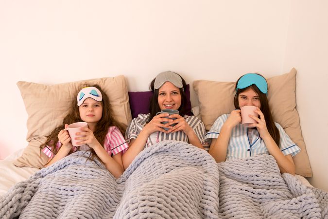 Family enjoying cozy morning with warm drinks in bed.