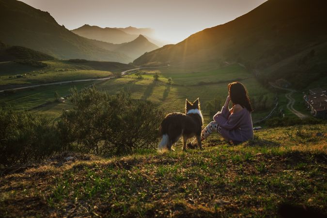 Adult tourist with dog against green forested valley under clear sky in summer