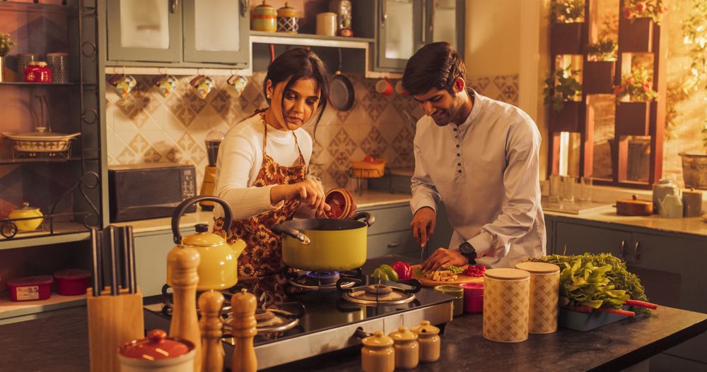 Playful Indian Couple Preparing Food in the Kitchen: Learning New Recipes, Laughing and Having Fun While Cooking.