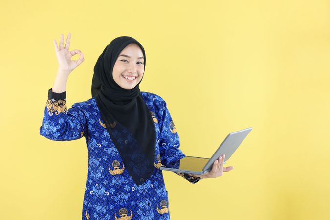 Female Indonesian Holding Laptop Computer with OK Gesture