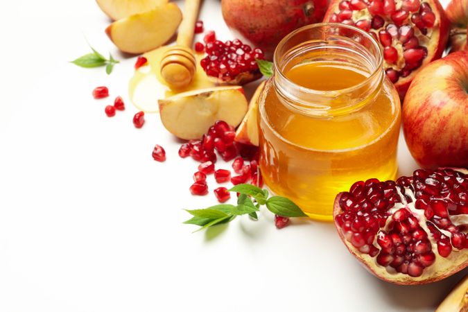 Top view of glass honey pot with pomegranate, and an apple quarters with copy space