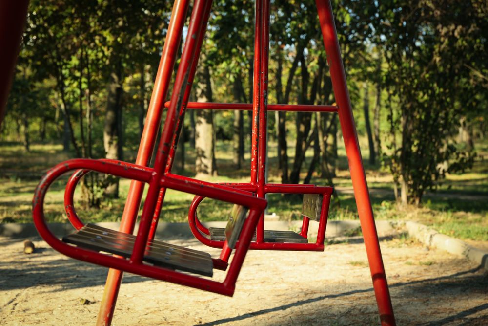 Red swings in city park in bright sunny morning