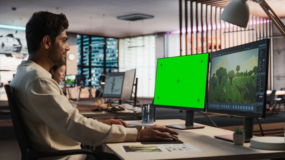 Indian Male Game Designer Using Desktop Computer With Green Screen Chromakey on Display, Designing Immersive World In 3D modelling Software For RPG Video Game.