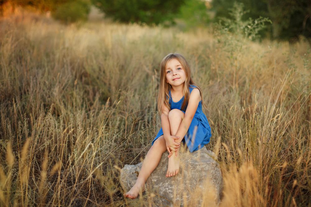 Female child sitting on bolder in field