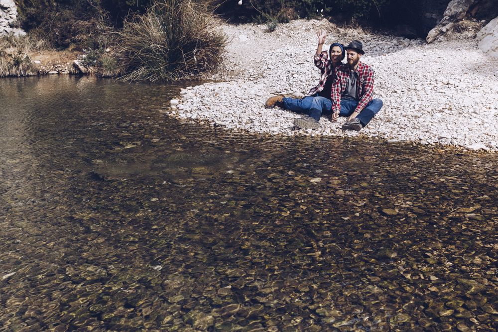Positive woman and man resting on stone shore near river
