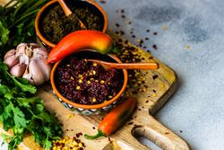 Pot of traditional Georgian sauce Adjika with garlic bulb & raw ingredient on wooden board
