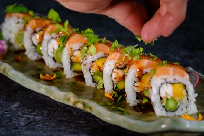 Crop person dressing delicious sushi on marble plate