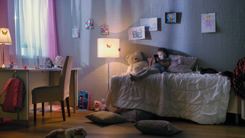 Cute Girl Lies on Her Bed and Watches Cartoons on a Smartphone.