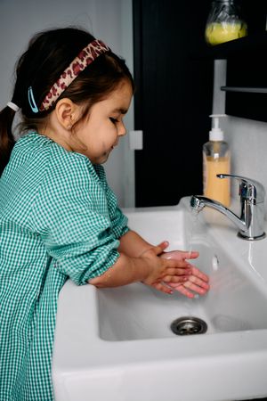 A little brunette girl with a green baby is washing her hands in the bathroom