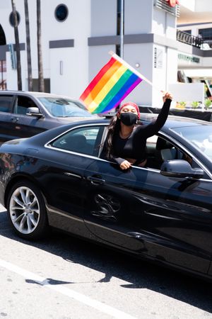 Los Angeles, CA, USA — June 14th, 2020: woman waves rainbow flag out of car window at BLM protest